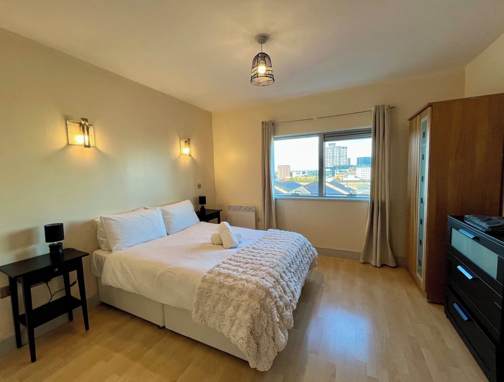 A hotel room with a bed, bedside tables, a wardrobe, a window with a city view, and a ceiling light.