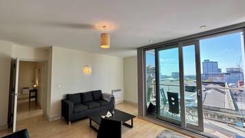 A modern living room with a black sofa, a coffee table, and a large window offering a city view.