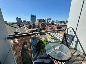 A balcony with a glass table and chairs, overlooking a cityscape with modern and historic buildings. - Free Carpark Modern Lux 2 Bedroom Apt City Centre (Manchester)