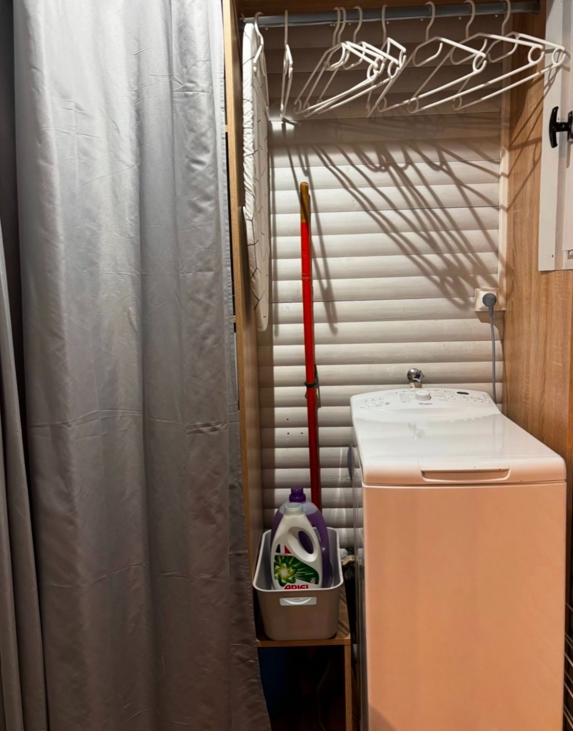 Un baño pequeño con lavadora, lavamanos, tendedero y escoba.