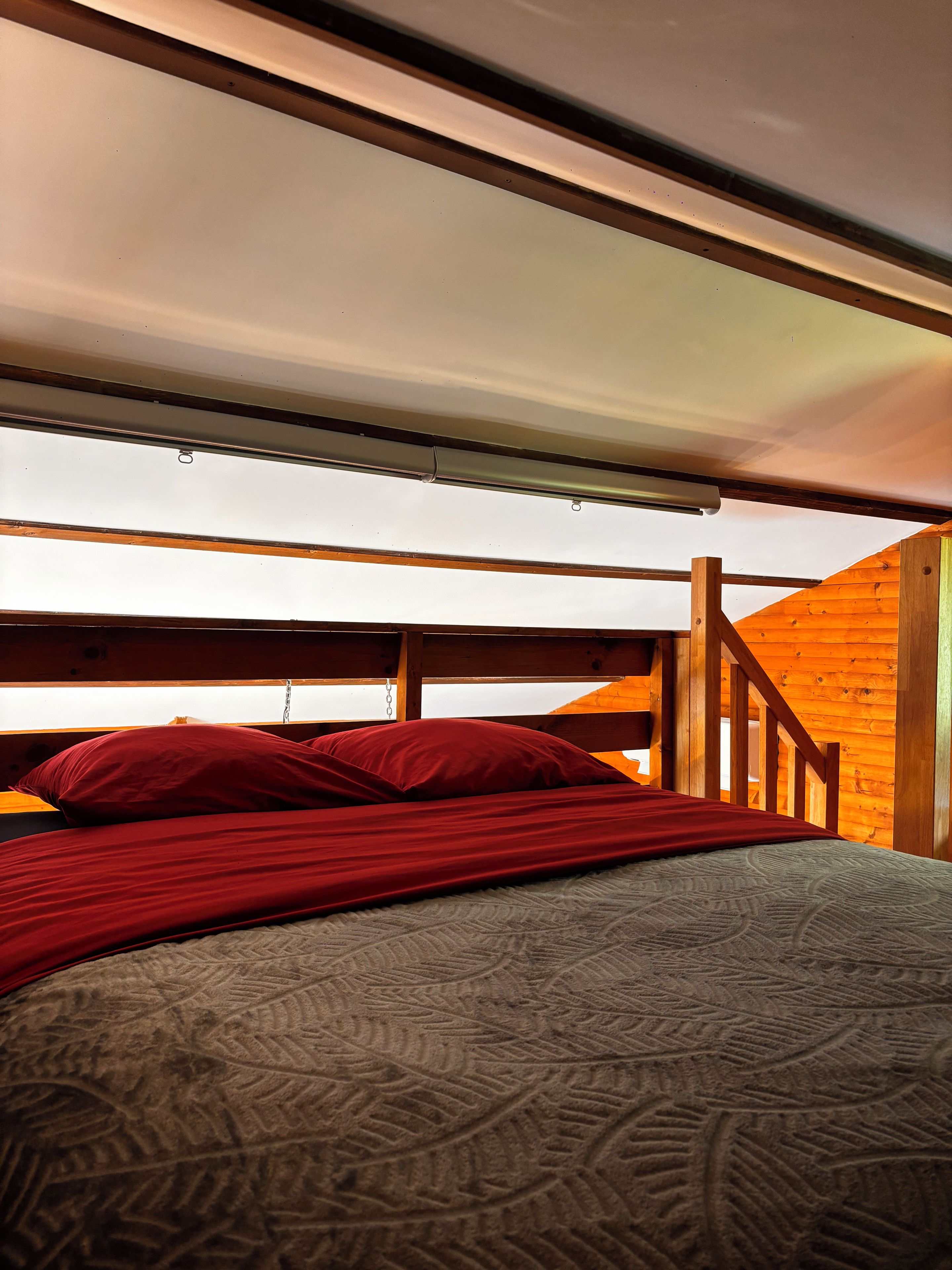Een stapelbed met rode beddengoed, een houten hoofdbord en uitzicht op een houten trap.
