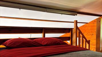 Een stapelbed met rode beddengoed, een houten hoofdbord en uitzicht op een houten trap.