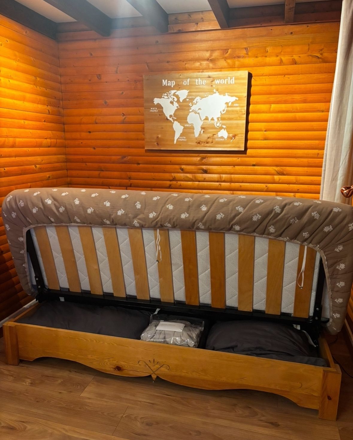 Interior de una cabaña de madera con sofá cama, un mapa mundial en la pared y suelo de madera.