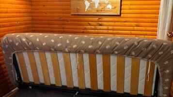 Interior de una cabaña de madera con sofá cama, un mapa mundial en la pared y suelo de madera.