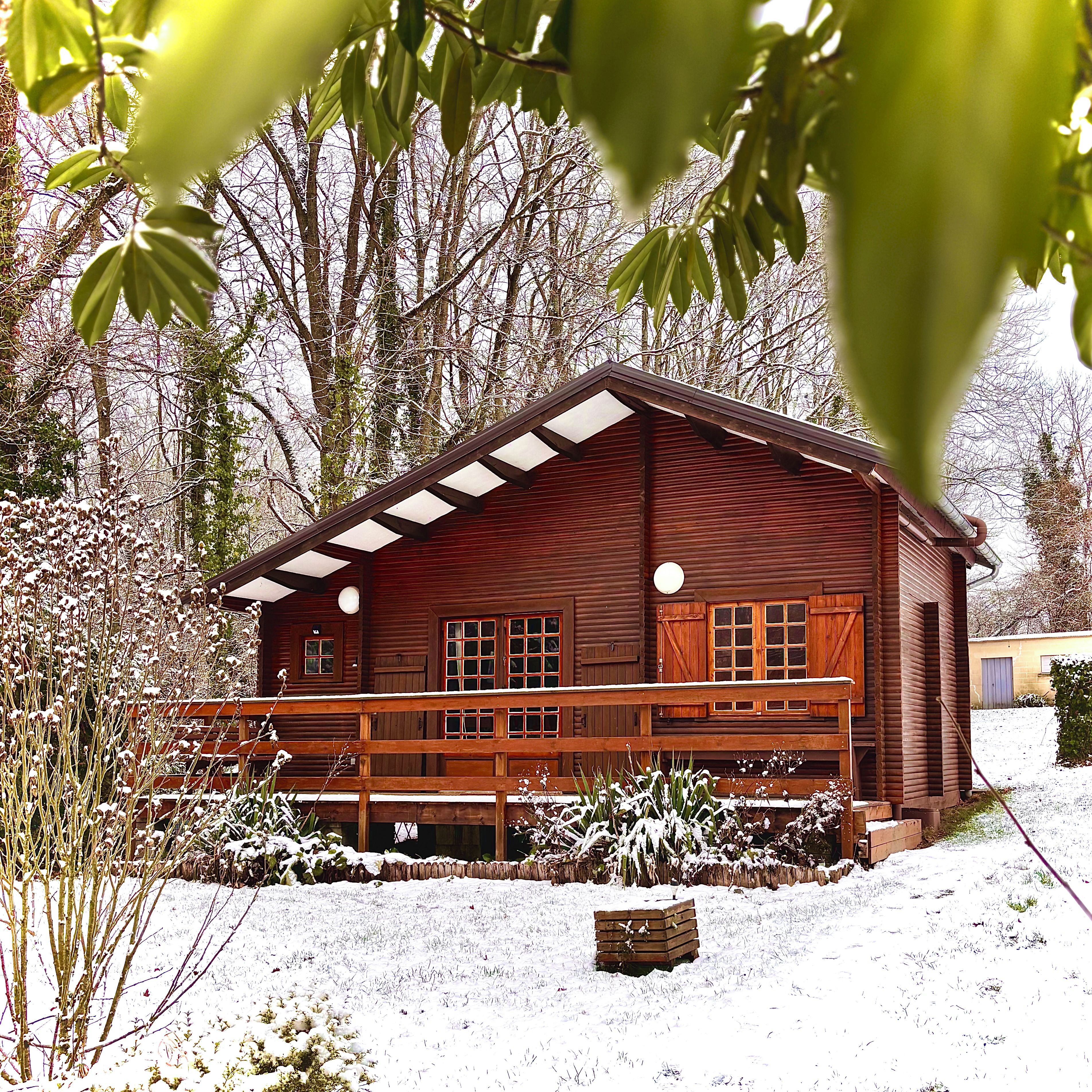 Una cabaña de madera con balcón, rodeada de suelo y árboles cubiertos de nieve.