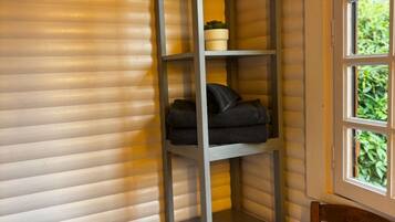 Una habitación de esquina con una estantería metálica gris, una silla de madera y un cesto de basura.