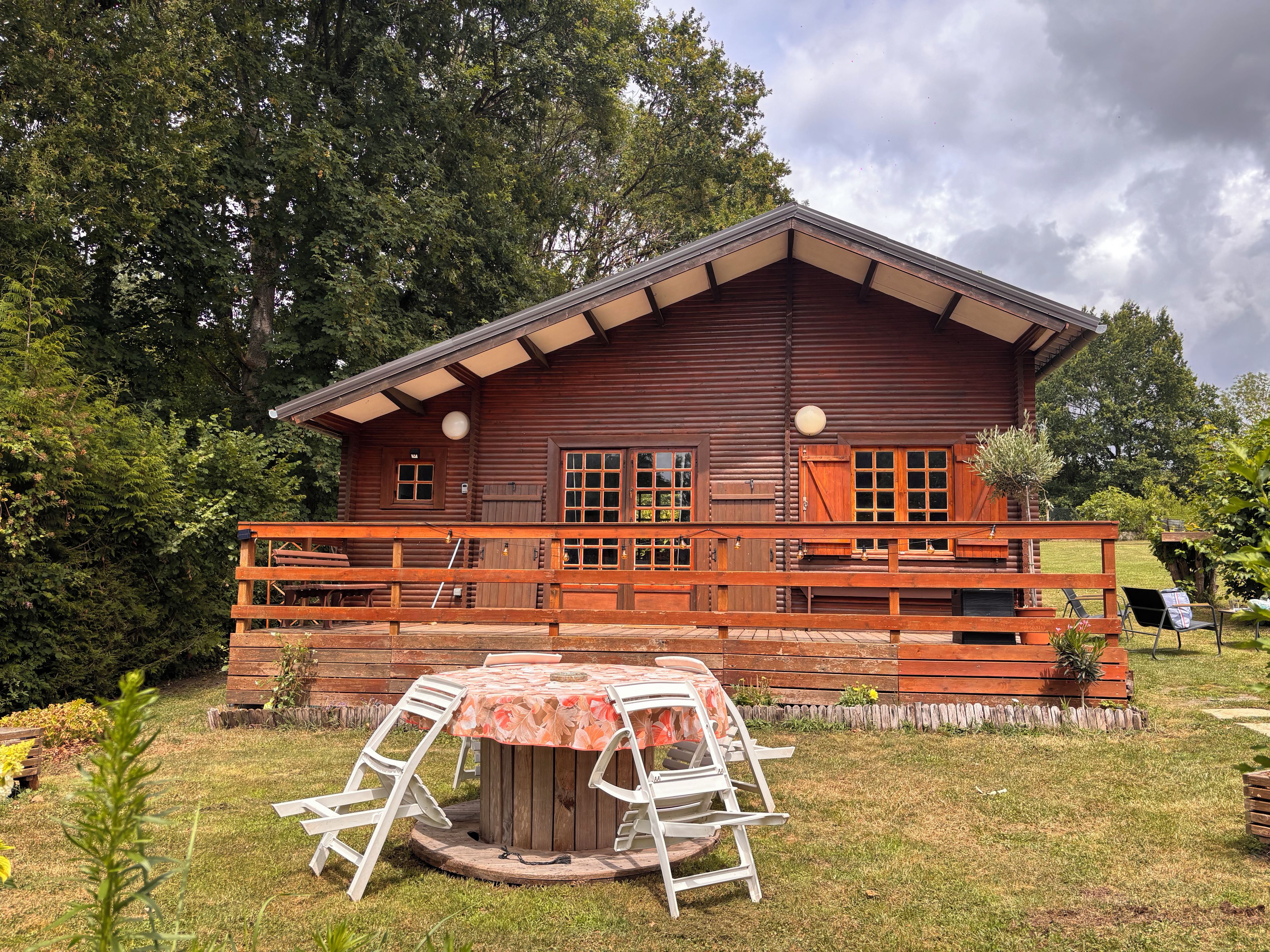 A wooden cabin with a porch, a round table with chairs, and a small garden area.
