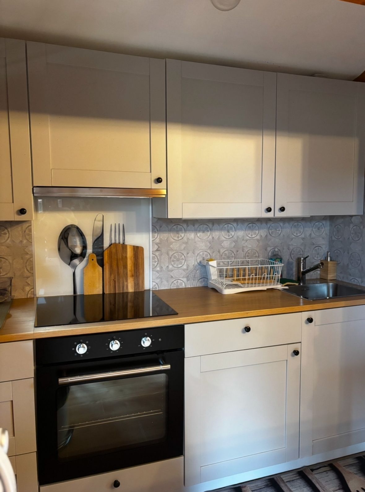 Eine Küche mit weißen Schränken, einem schwarzen Backofen und einer Holzausziehtafel.