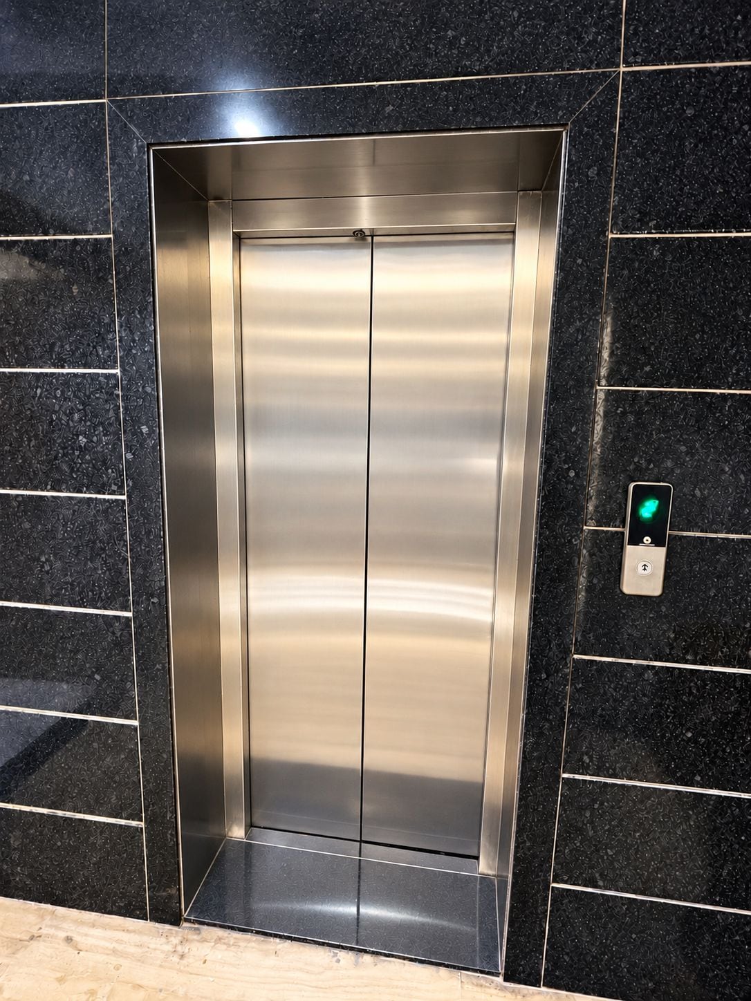 Un ascensor metálico con un botón verde en la pared a su lado.