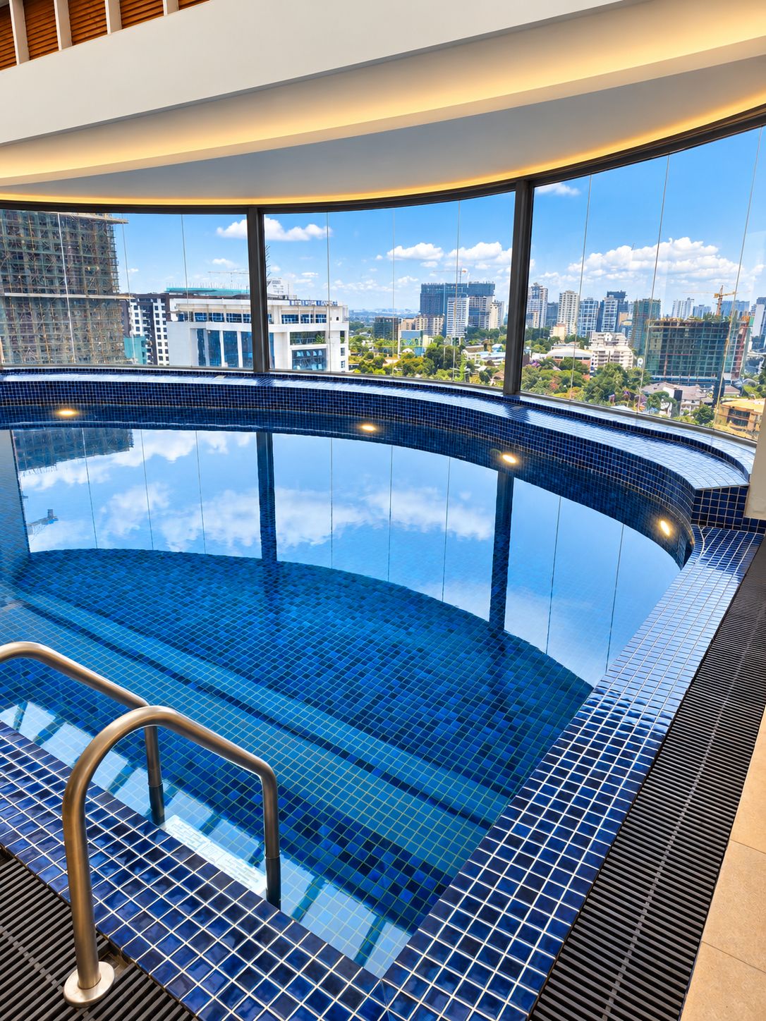 Ein moderner, überdachter Pool mit gebogenem Design, großen Fenstern und Stadtblick sowie einer Metallleiter zum Zugang.