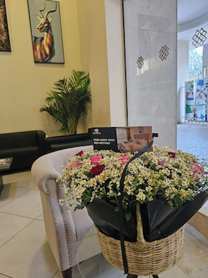 Una zona de recepción con una cesta de mimbre que contiene un ramo de flores, un letrero negro con la marca 'Bed'n Beyond' y una obra de arte enmarcada en la pared.