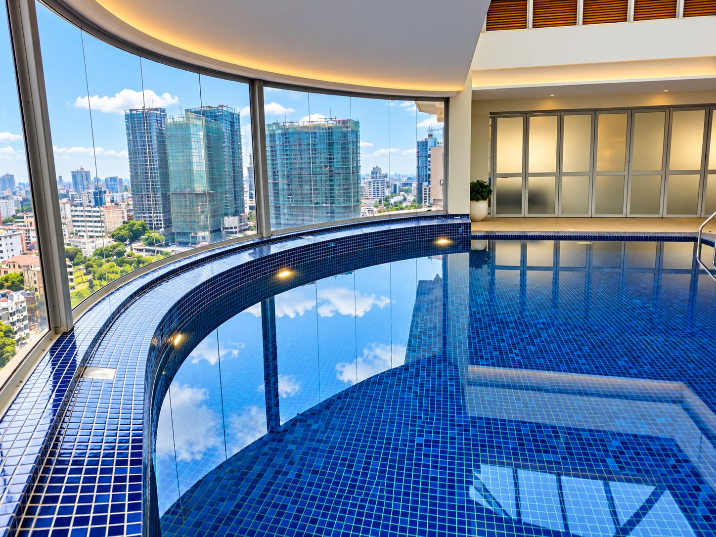 Ein modernes Hallenbad mit geschwungenem Design, großen Fenstern und Stadtblick sowie einem minimalistischen Innenraum.