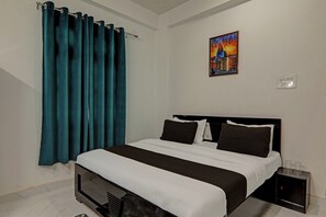 Une chambre d’hôtel avec un lit, une table de chevet, une lampe, un tableau au mur et des rideaux de couleur turquoise.