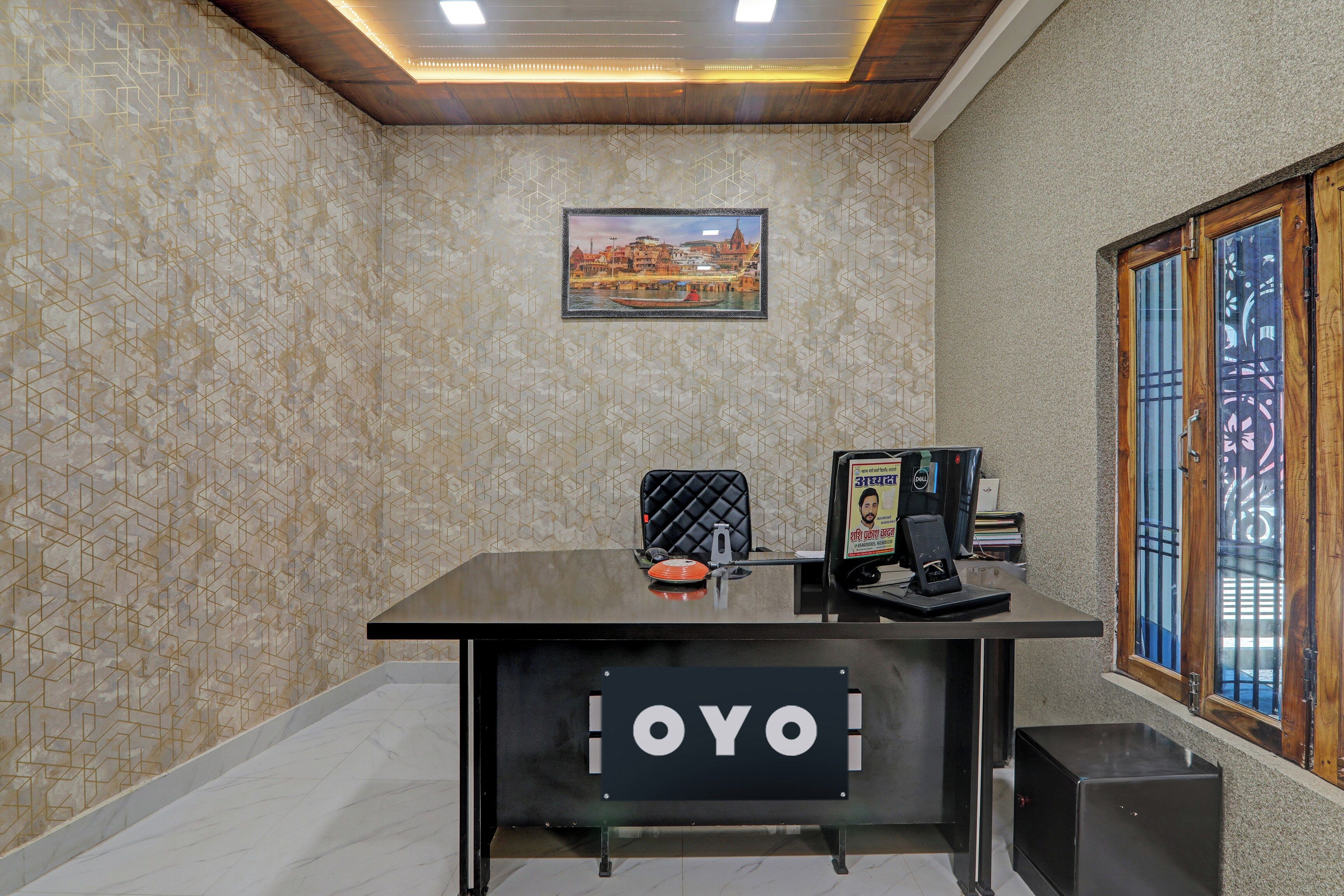 Un comptoir d'accueil avec une enseigne indiquant « OYO », dans une pièce dont les murs sont recouverts d'un papier peint à motifs et où est accroché un tableau représentant un paysage urbain.