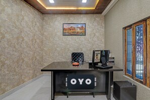 Un comptoir d'accueil avec une enseigne indiquant « OYO », dans une pièce dont les murs sont recouverts d'un papier peint à motifs et où est accroché un tableau représentant un paysage urbain.