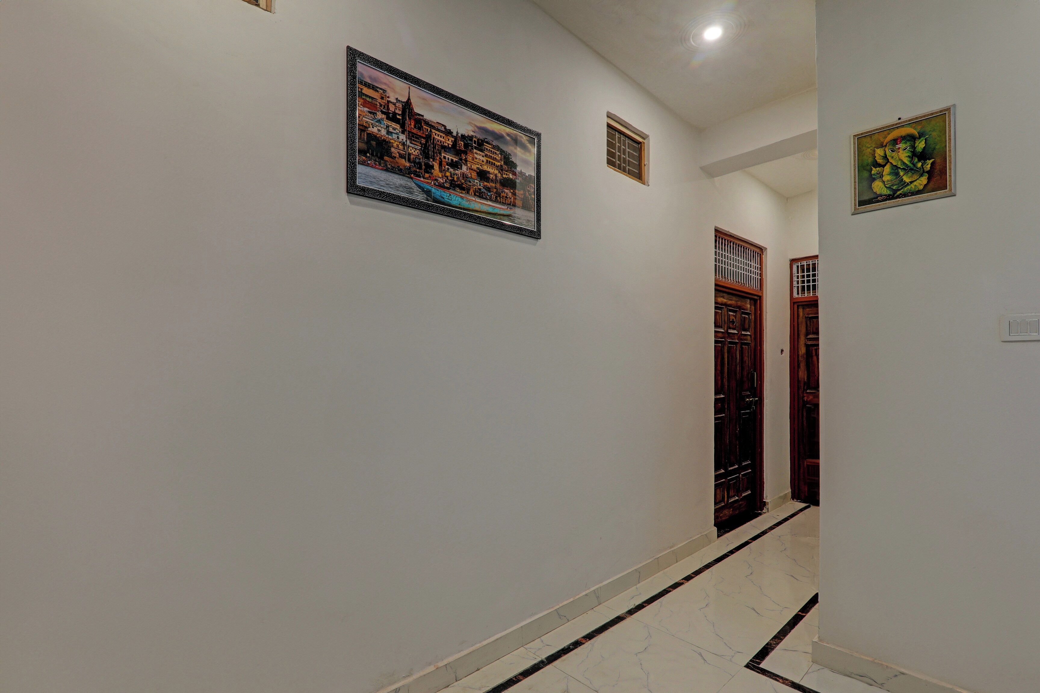 A hallway with a framed cityscape painting, a door with a barred window, and a small decorative item on the wall.