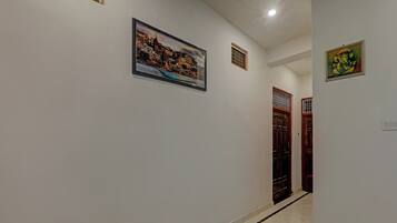 A hallway with a framed cityscape painting, a door with a barred window, and a small decorative item on the wall.