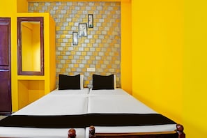 A double bed with white bedding and black pillows in a room with yellow walls and a brick-patterned accent wall. - Hotel O Sivaganga Guest House (Trivandrum)