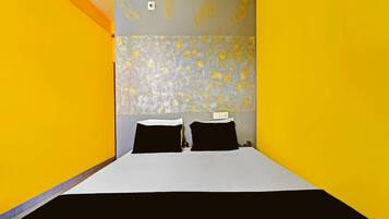 Een hotelkamer met een bed, twee zwarte kussens, een wit sprei en een gestreept hoofdbord.