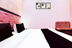 Una habitación de hotel con una cama grande, cabecera, zona de estar y tres obras de arte colgadas en la pared.