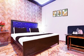 Une chambre d’hôtel avec un lit, une table de chevet, un vase de fleurs et un mur recouvert d’un papier peint à motifs, ainsi que trois tableaux encadrés.