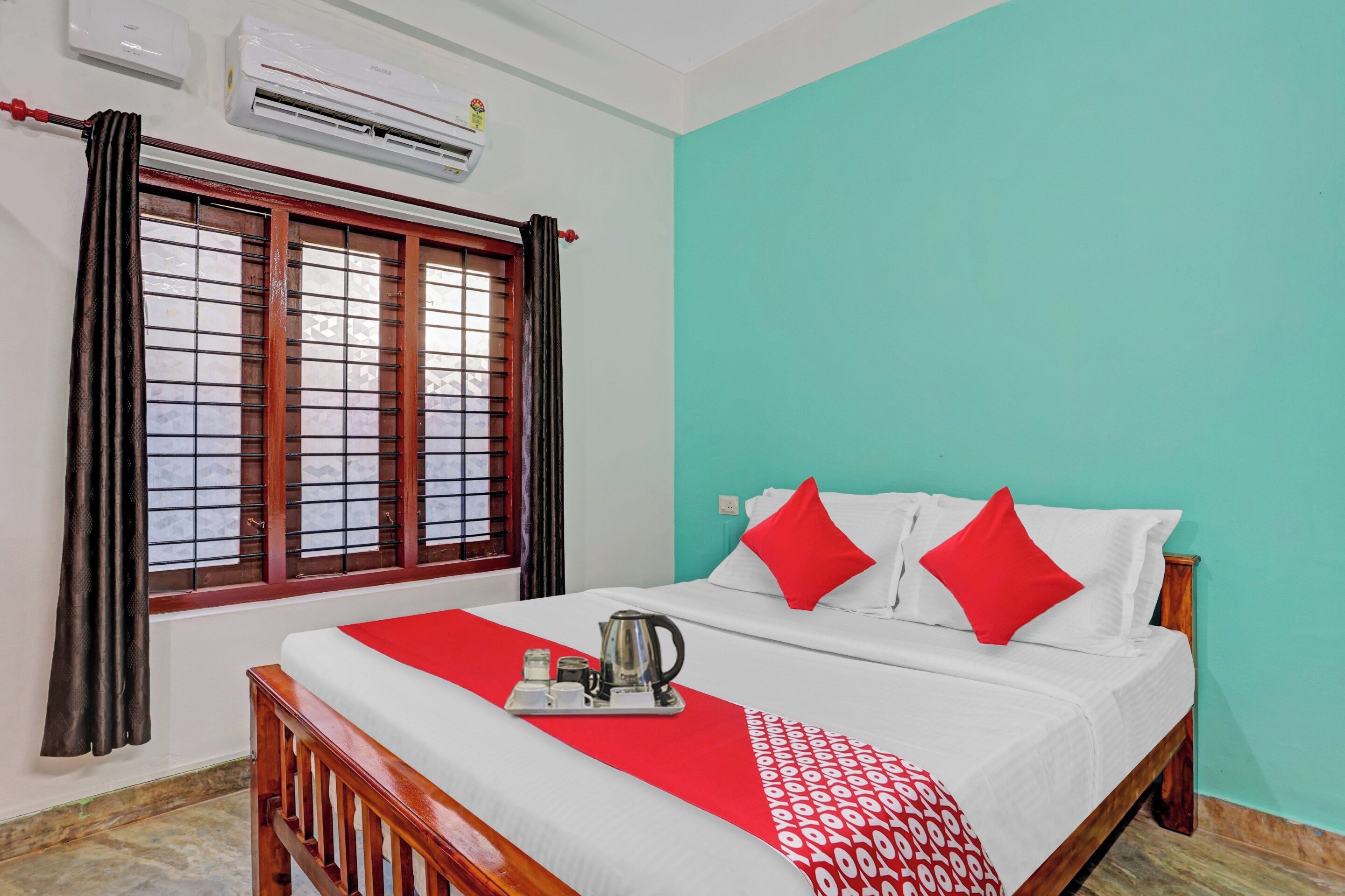A hotel room with a bed, a window with curtains, an air conditioner, and a teal wall.
