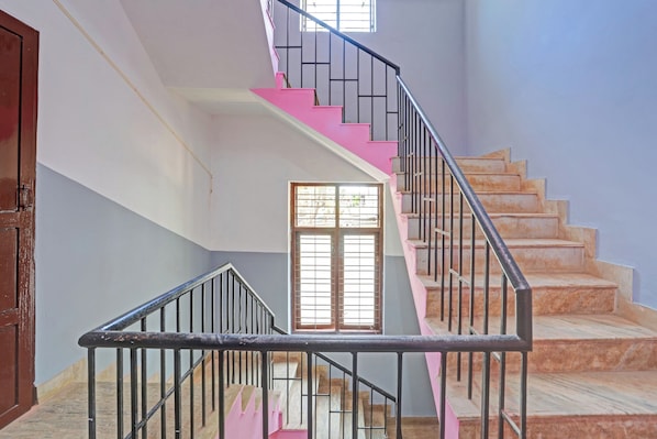 Una escalera con escalones rosas y barandillas negras, que lleva a un rellano con una ventana.