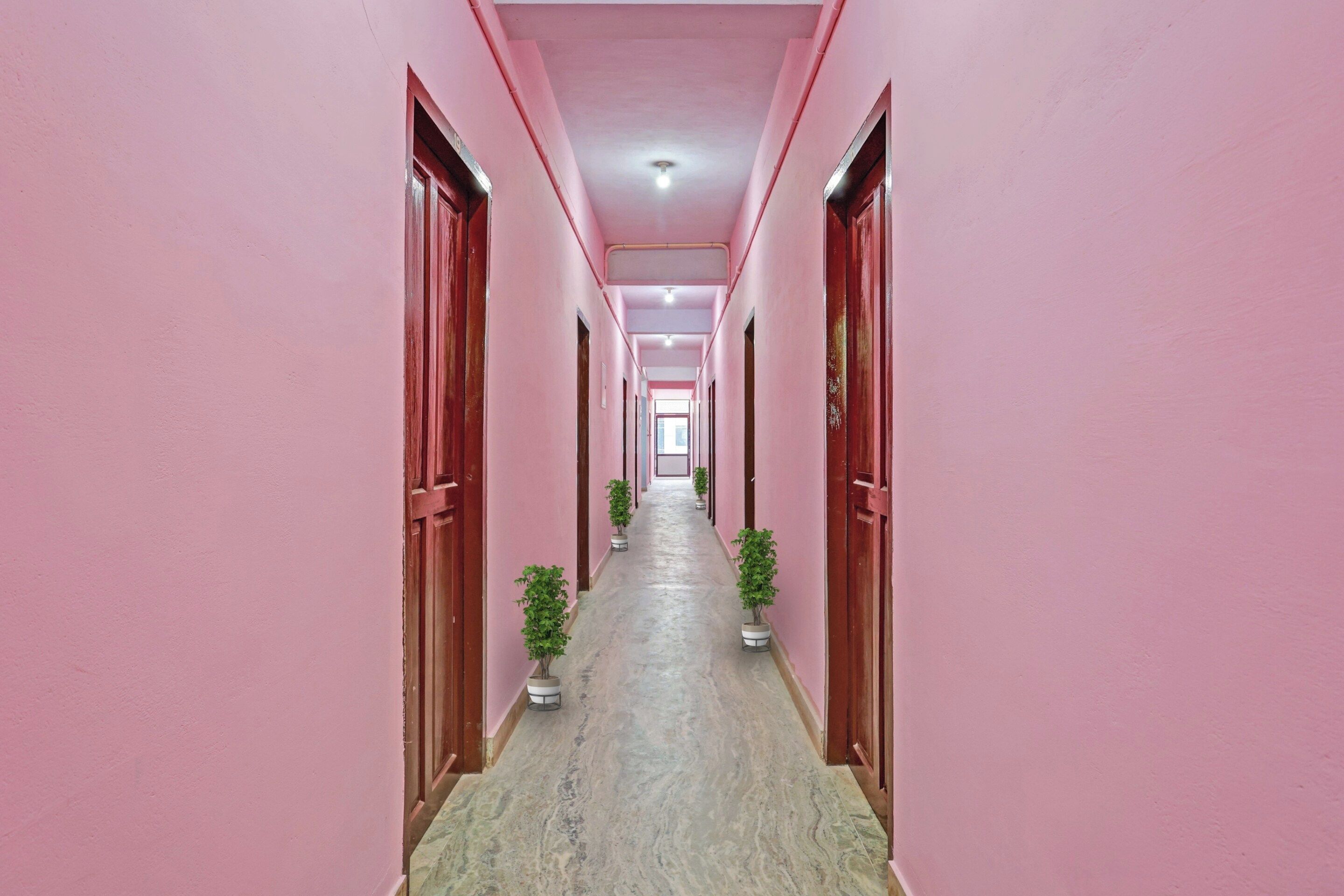 Um corredor com paredes e portas rosa, que leva a um quarto claro no final.