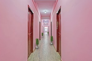 Un pasillo con paredes rosas y puertas, que conduce a una habitación luminosa al final.