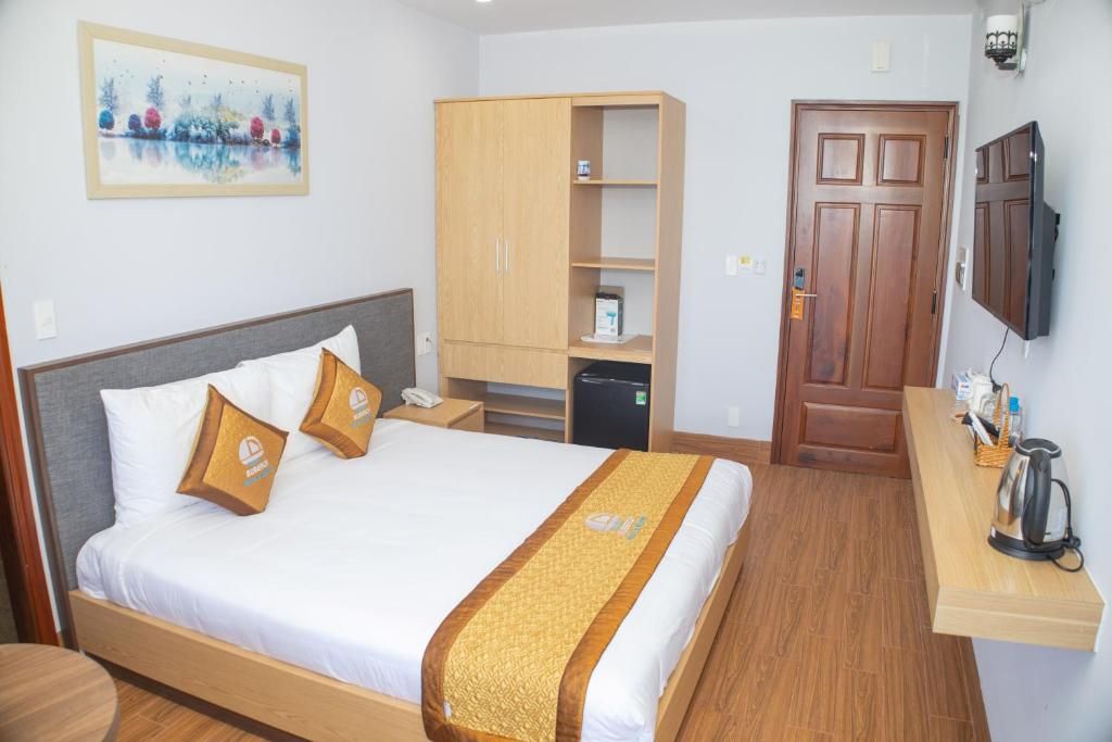 Habitación de hotel con cama, armario, escritorio con hervidor y televisión en la pared.