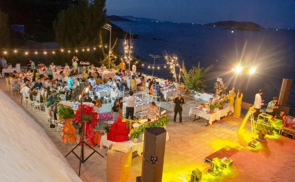 An outdoor event with tables and chairs arranged for guests, set against a backdrop of a body of water and hills.