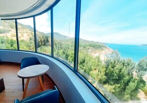 Una habitación con pared curva y ventanas amplias que ofrecen vistas al litoral y colinas.