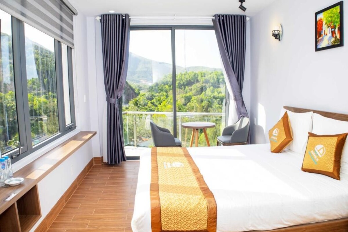 Une chambre d’hôtel avec un grand lit, un balcon avec vue, une petite table et une chaise.
