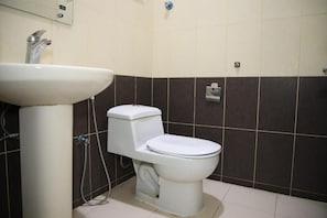 Un baño con lavamanos blanco, inodoro y paredes de baldosas marrón oscuro.