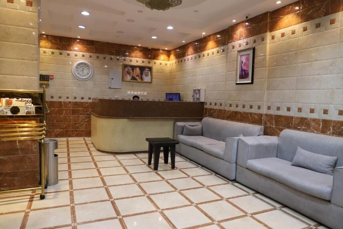 Un hall con mostrador de recepción, un sofá, un cubo de basura y un reloj en la pared.