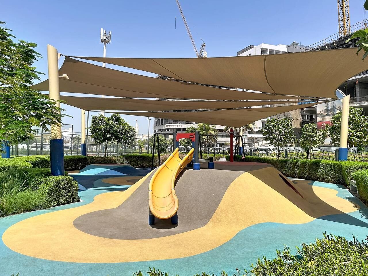 A playground with a slide, surrounded by greenery and a shaded area.