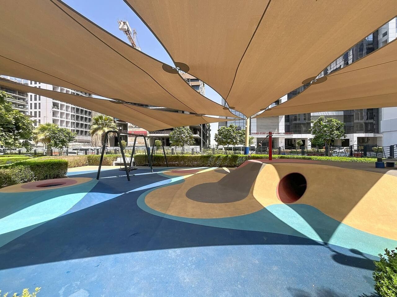 A playground with a slide and climbing structures, surrounded by buildings and greenery.