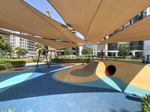 Un terrain de jeux avec un toboggan et des structures d’escalade, entouré de bâtiments et de verdure.
