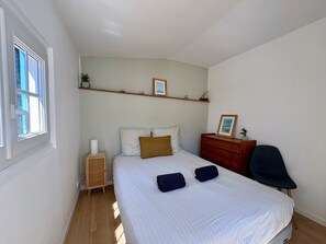 Un dormitorio con cama, mesita de noche, silla y ventana.