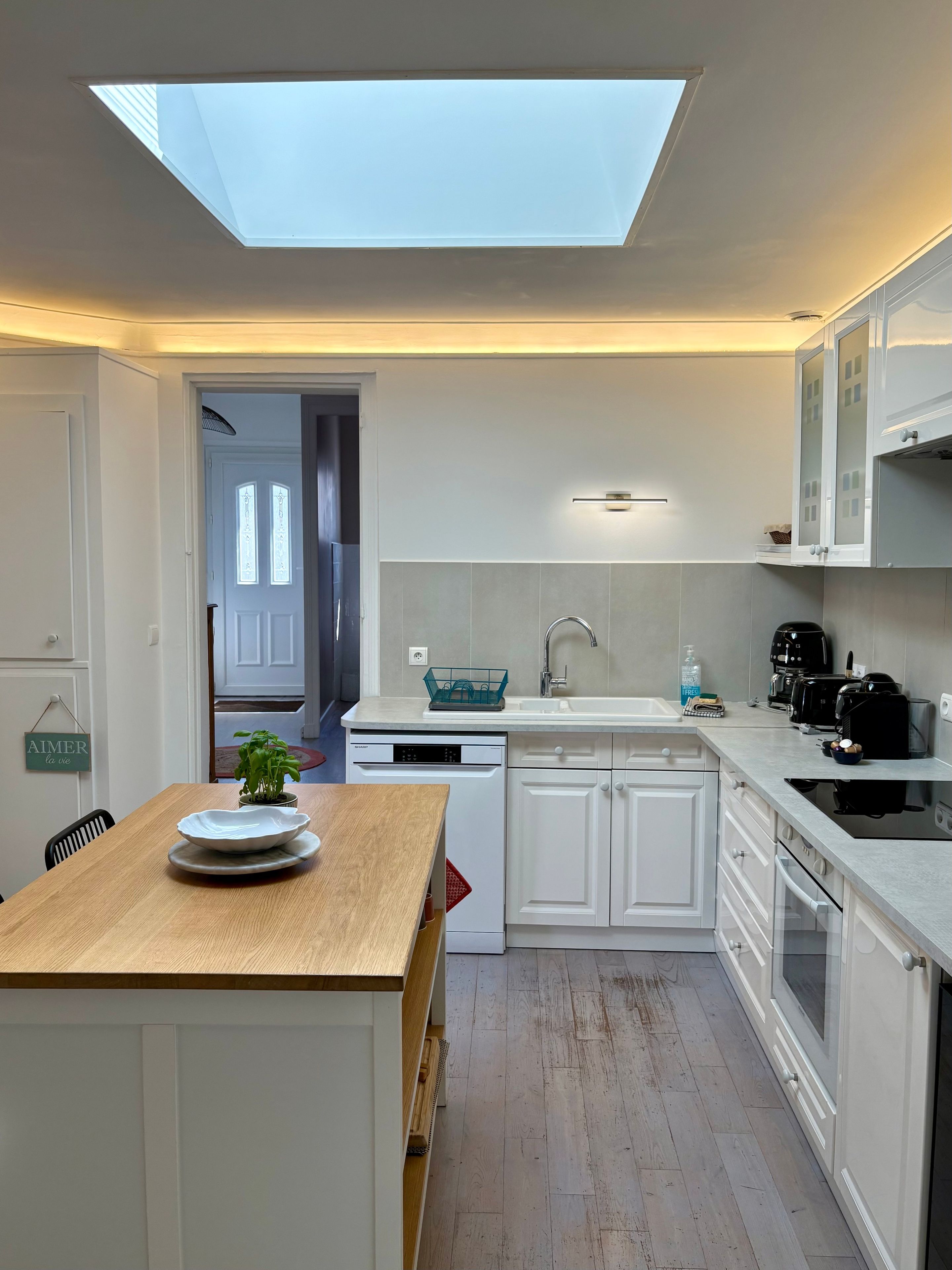 A modern kitchen with a skylight, white cabinetry, and a wooden dining table.