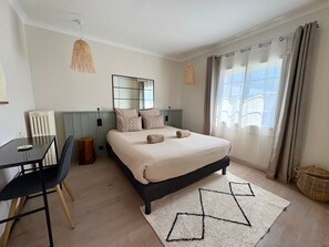 Ein Schlafzimmer mit einem Bett, einem Schreibtisch, einem Stuhl, einem Fenster mit Vorhängen und einer Pendelleuchte.