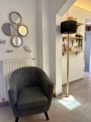Ein Zimmer mit grauem Sessel, einer Stehlampe und wandmontierten Spiegeln.