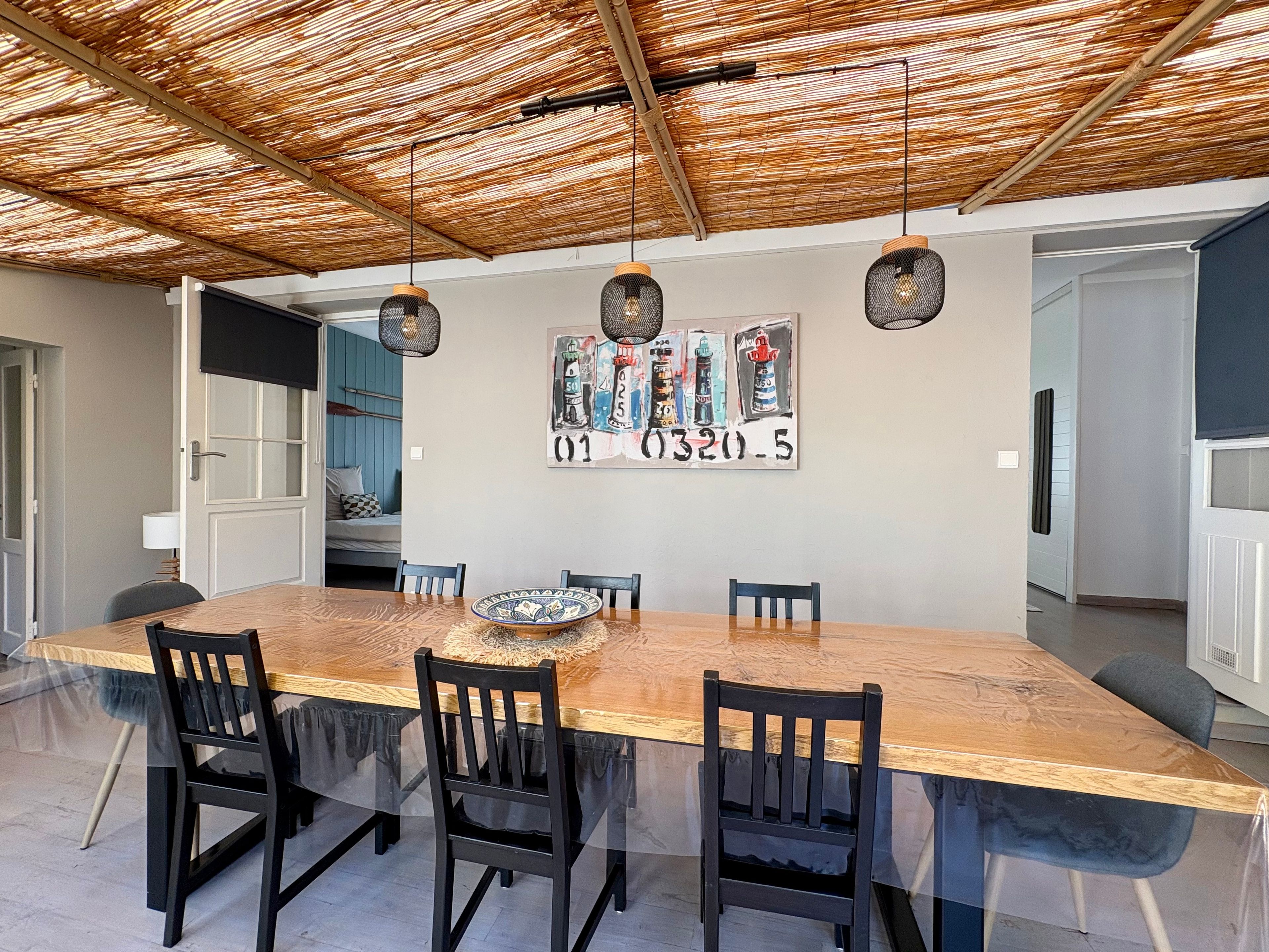 A dining area with a large wooden table, black chairs, and a woven ceiling.