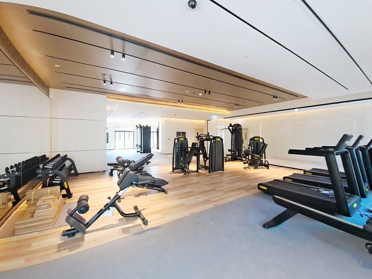 A gym with various exercise equipment, including treadmills and weight machines, arranged in a spacious room with wooden flooring and a high ceiling.