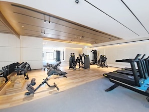 Une salle de sport équipée de divers appareils d’exercice, notamment des tapis de course et des appareils de musculation, disposés dans un espace vaste doté d’un plancher en bois et d’un plafond haut.