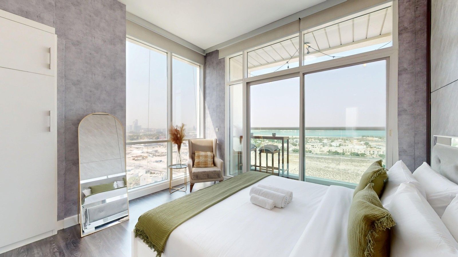 A modern hotel room with a large bed, a chair, a small table, and a view of the beach.