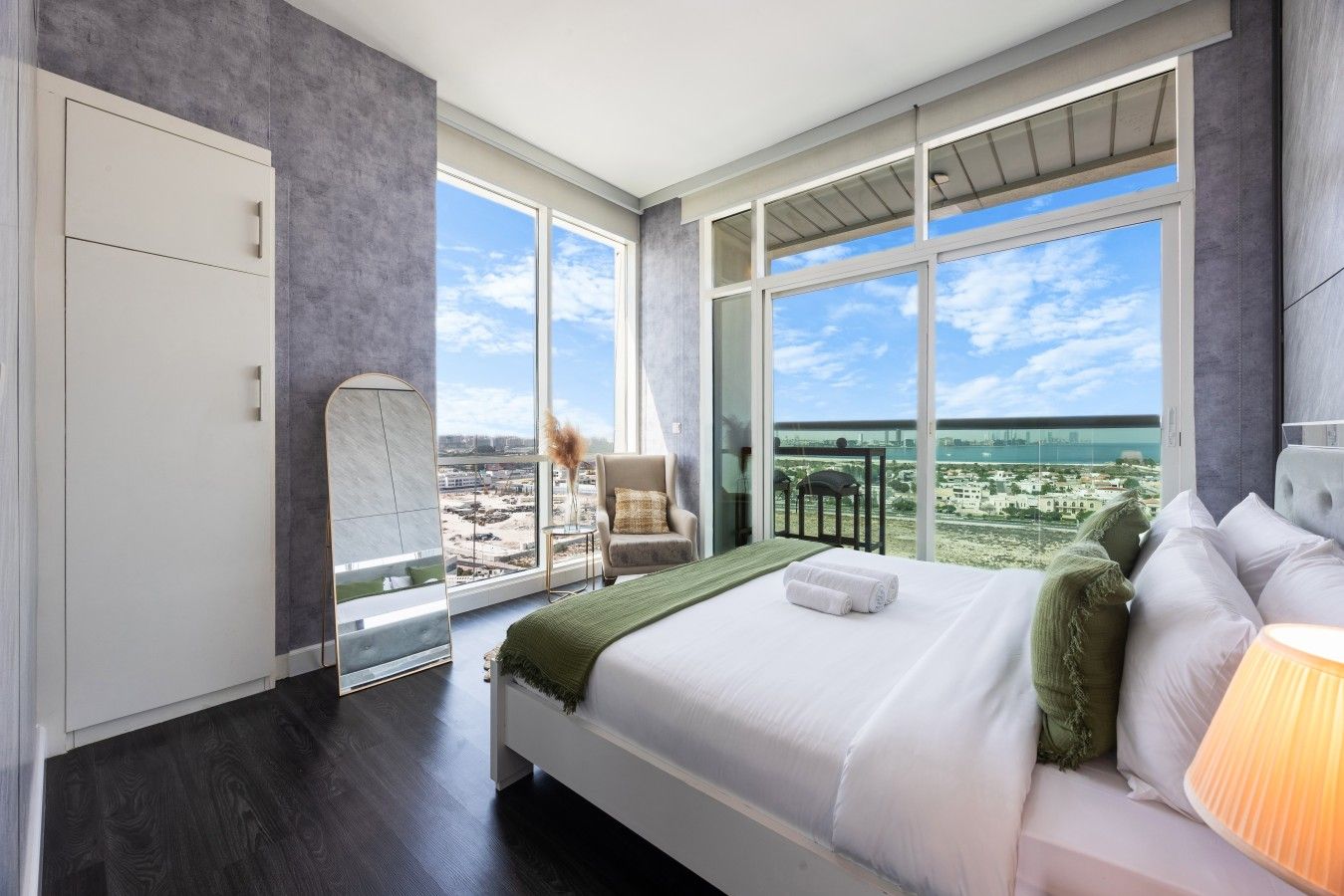 A modern hotel room with a large bed, a seating area, and a balcony with a city view.