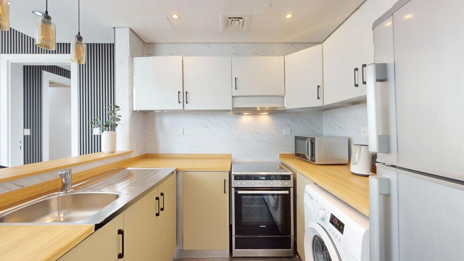 Une cuisine moderne avec des meubles blancs, un évier en acier inoxydable, un four encastré et un lave-linge.