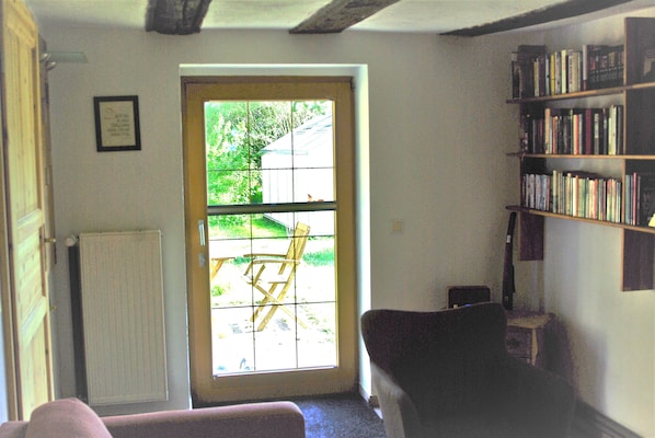 Une pièce avec une porte donnant sur l’extérieur, un radiateur, une bibliothèque et une chaise.