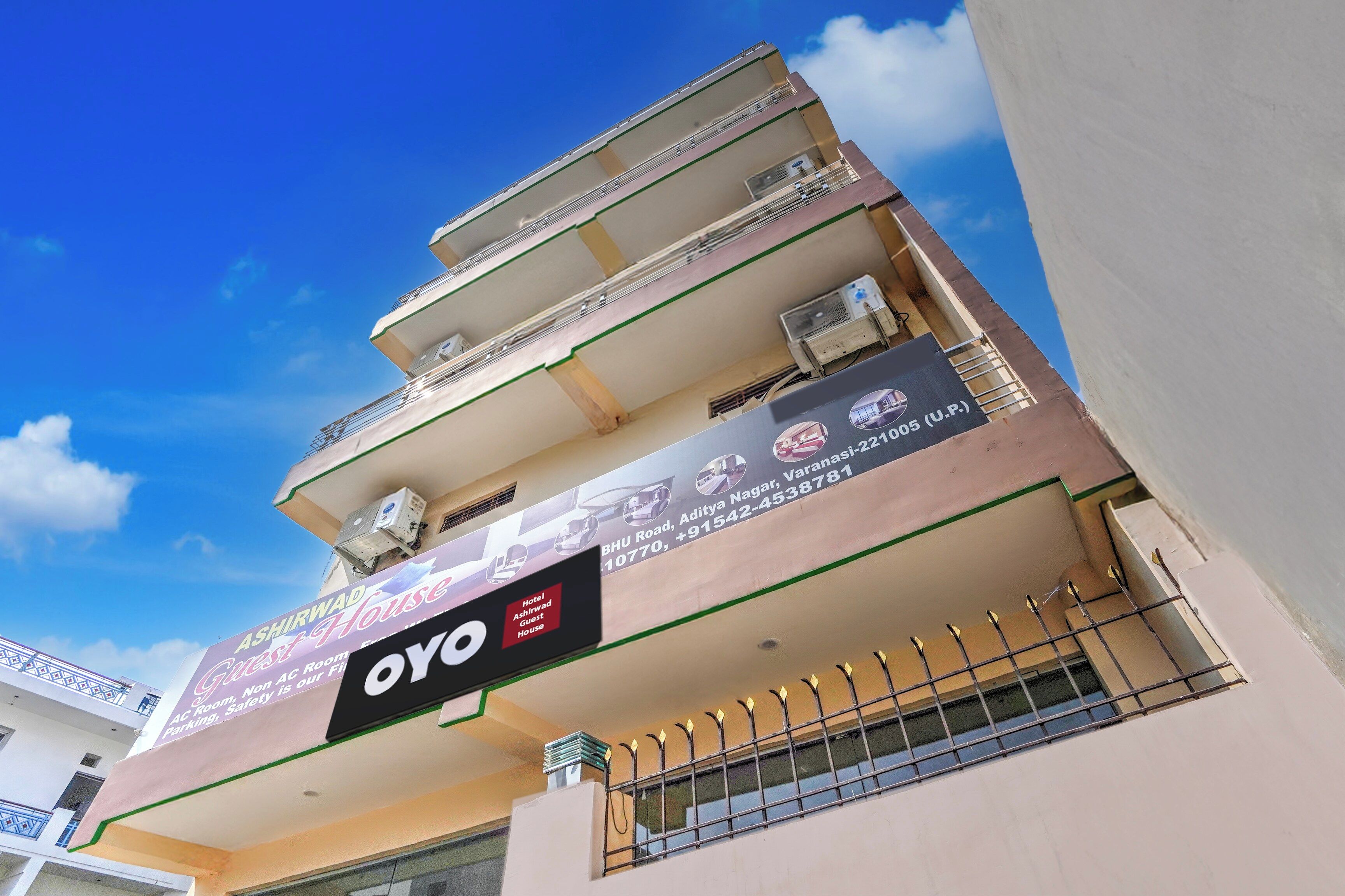 A multi-story building with balconies, a sign for 'Hotel Ashirwad Guest House,' and an 'OYO' branding.